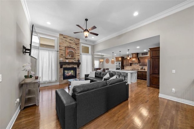 living room with dark wood-type flooring, ceiling fan, ornamental molding, and a fireplace