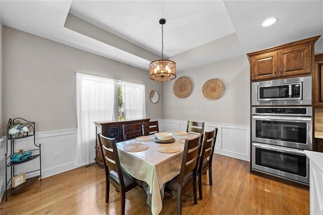 dining room with a raised ceiling, light hardwood / wood-style flooring, and a notable chandelier