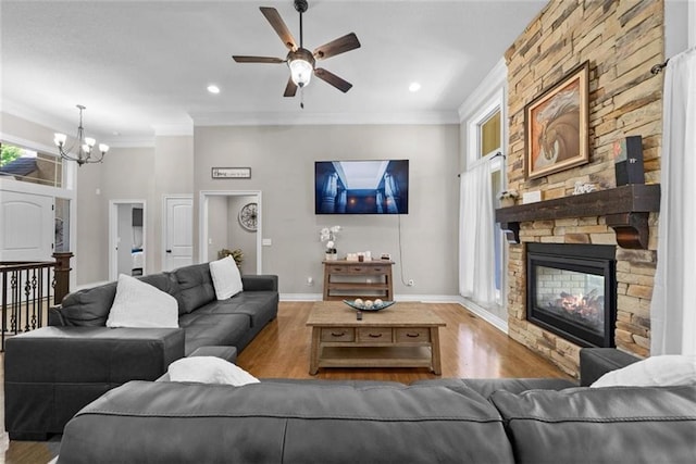 living room featuring ornamental molding, a stone fireplace, hardwood / wood-style floors, and ceiling fan with notable chandelier