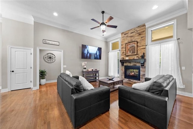 living room featuring crown molding, ceiling fan, wood-type flooring, and a stone fireplace