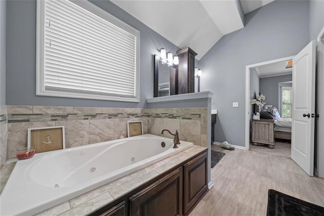 bathroom with lofted ceiling, vanity, and tiled tub