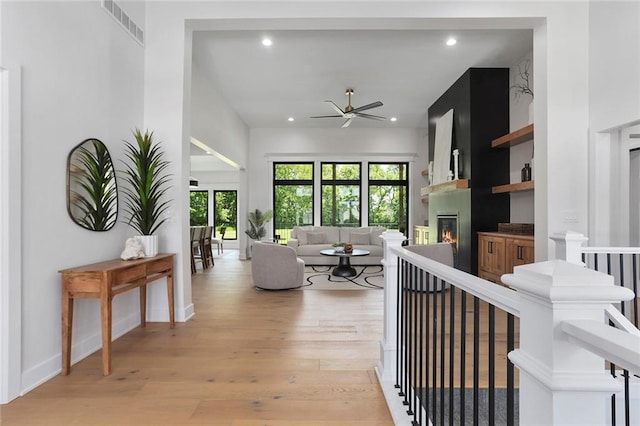 living room with ceiling fan, a large fireplace, and light wood-type flooring