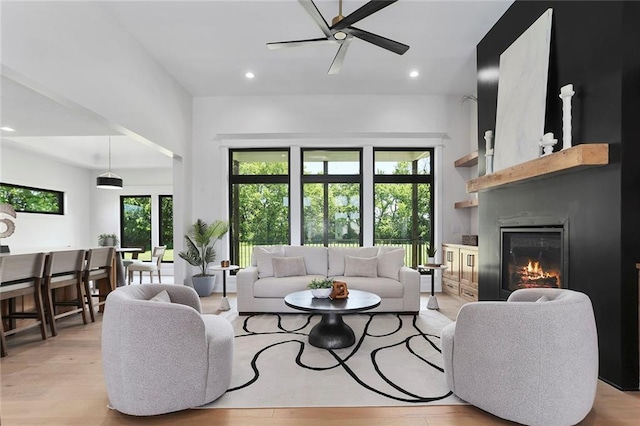 living room with ceiling fan, a large fireplace, and light wood-type flooring