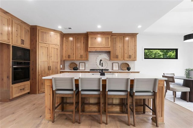 kitchen with a kitchen bar, a spacious island, light hardwood / wood-style flooring, and black appliances