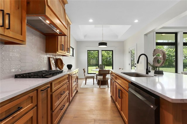 kitchen with appliances with stainless steel finishes, custom range hood, pendant lighting, light hardwood / wood-style flooring, and an island with sink