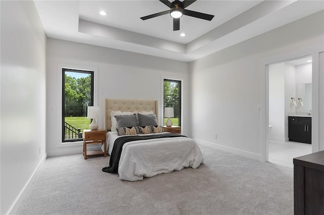 bedroom featuring multiple windows, light colored carpet, ensuite bath, and ceiling fan