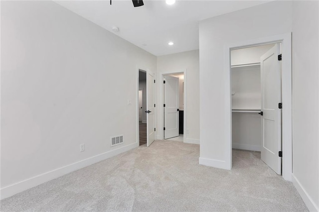 unfurnished bedroom with a walk in closet, light colored carpet, a closet, and ceiling fan