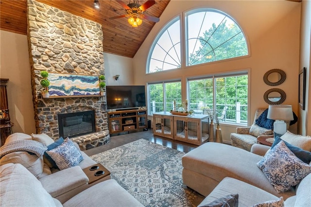 living room featuring wood ceiling, wood-type flooring, high vaulted ceiling, a stone fireplace, and ceiling fan