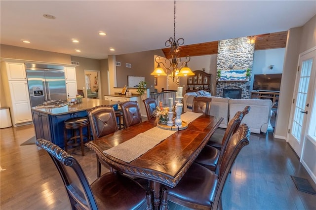 dining area with a notable chandelier, dark wood-type flooring, and a stone fireplace