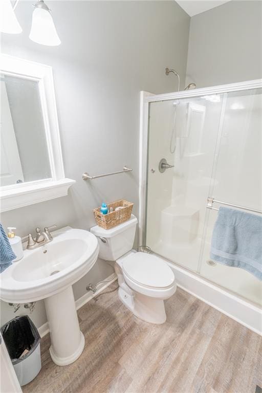 bathroom with hardwood / wood-style floors, a shower with shower door, and toilet