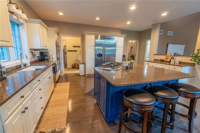 kitchen featuring appliances with stainless steel finishes, dark stone countertops, white cabinets, dark hardwood / wood-style floors, and sink