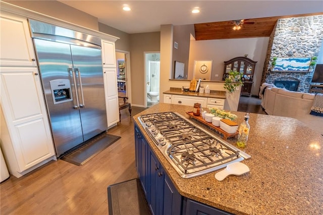 kitchen featuring light hardwood / wood-style floors, stainless steel built in fridge, a stone fireplace, ceiling fan, and blue cabinetry