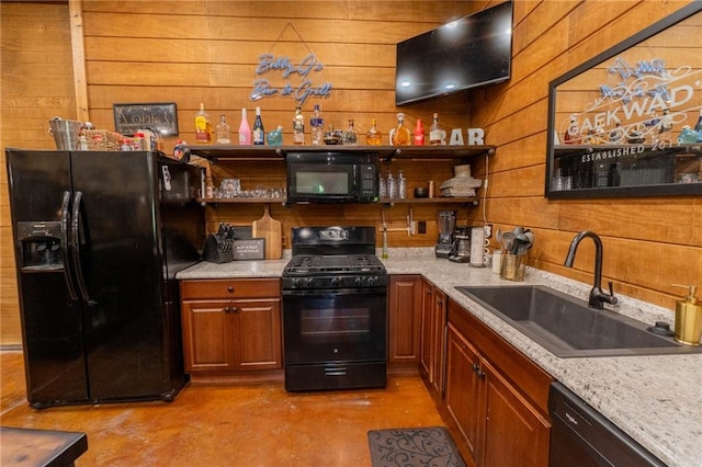 kitchen with wooden walls, black appliances, light stone counters, and sink