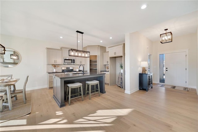 kitchen featuring gray cabinetry, pendant lighting, a kitchen island with sink, light hardwood / wood-style floors, and stainless steel appliances