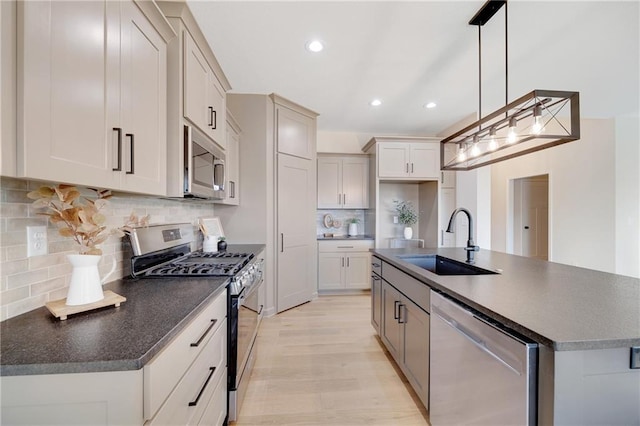 kitchen featuring decorative light fixtures, stainless steel appliances, a kitchen island with sink, and sink