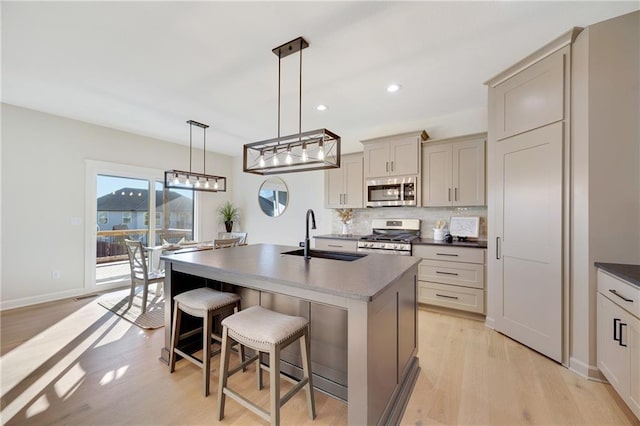 kitchen featuring sink, hanging light fixtures, light hardwood / wood-style flooring, a center island with sink, and appliances with stainless steel finishes