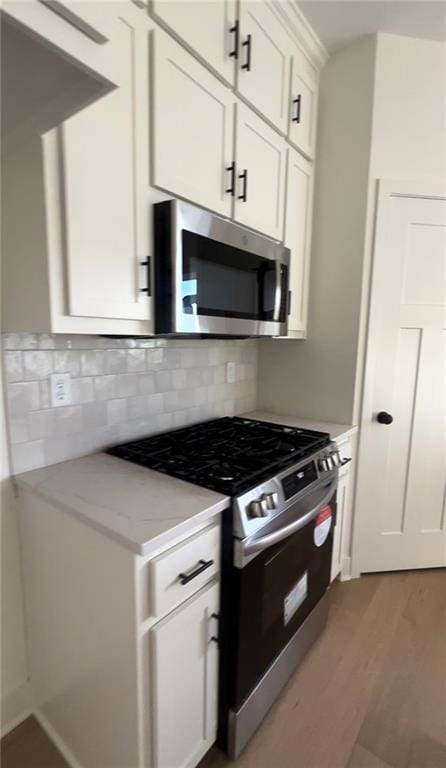 kitchen with white cabinetry, stainless steel appliances, light hardwood / wood-style floors, tasteful backsplash, and light stone counters