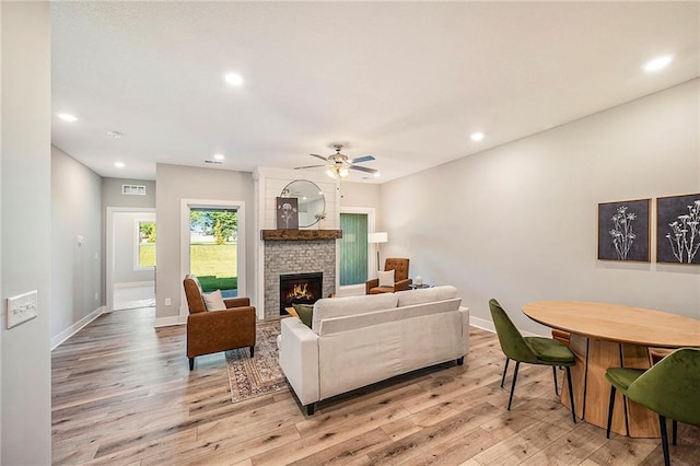 living room featuring a fireplace, light hardwood / wood-style floors, and ceiling fan