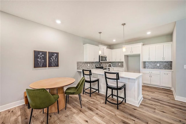 kitchen with hanging light fixtures, stainless steel appliances, kitchen peninsula, a kitchen bar, and white cabinets