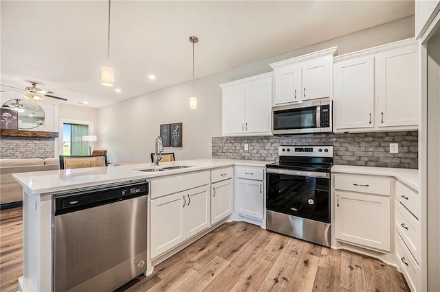 kitchen with kitchen peninsula, appliances with stainless steel finishes, decorative light fixtures, and white cabinets