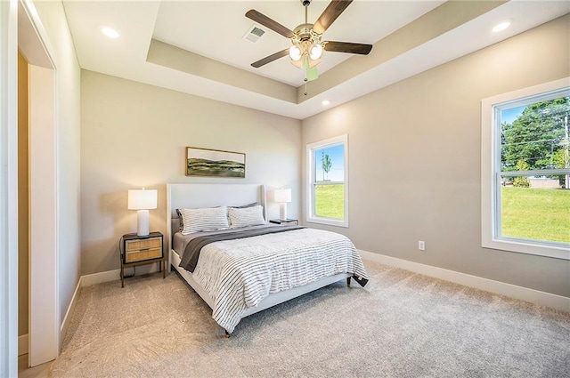 bedroom featuring a tray ceiling, multiple windows, ceiling fan, and carpet floors