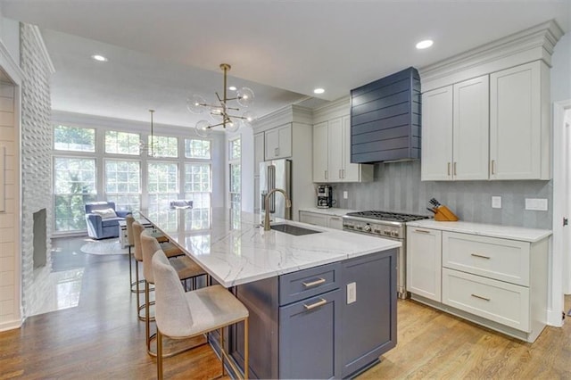 kitchen with pendant lighting, premium range hood, a center island with sink, sink, and stainless steel appliances