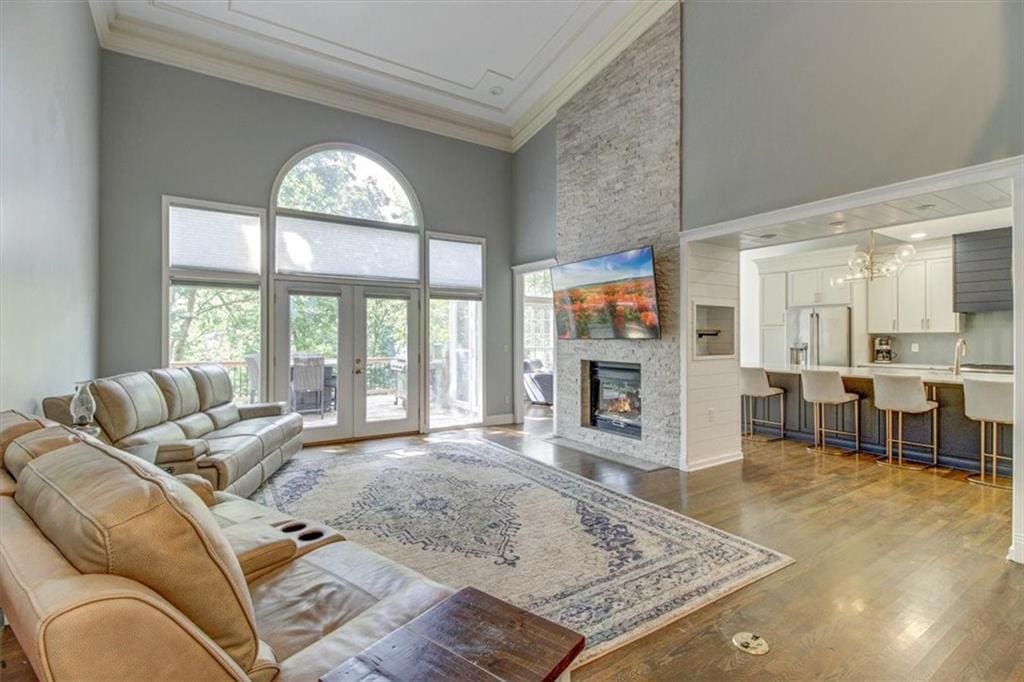 living room featuring crown molding, a towering ceiling, wood-type flooring, a stone fireplace, and french doors