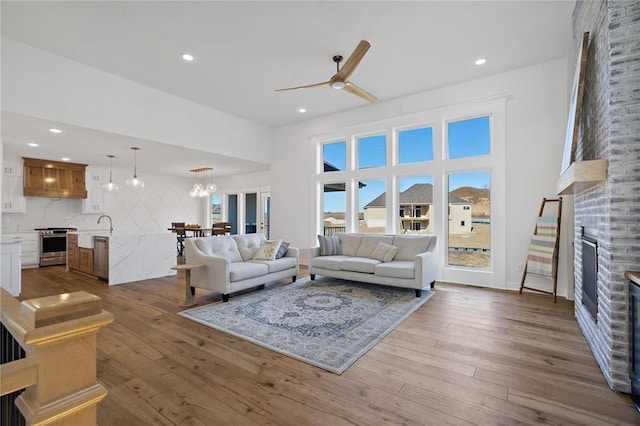 living room with ceiling fan with notable chandelier, a stone fireplace, and wood-type flooring