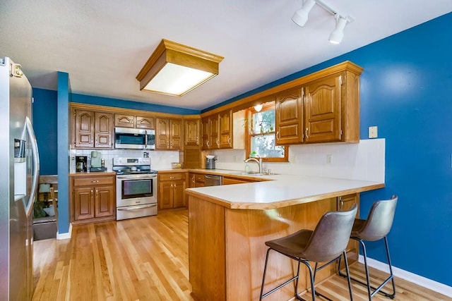 kitchen with appliances with stainless steel finishes, sink, a breakfast bar area, kitchen peninsula, and light hardwood / wood-style flooring