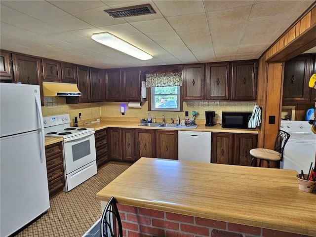 kitchen with white appliances, washer / dryer, dark brown cabinetry, sink, and tasteful backsplash