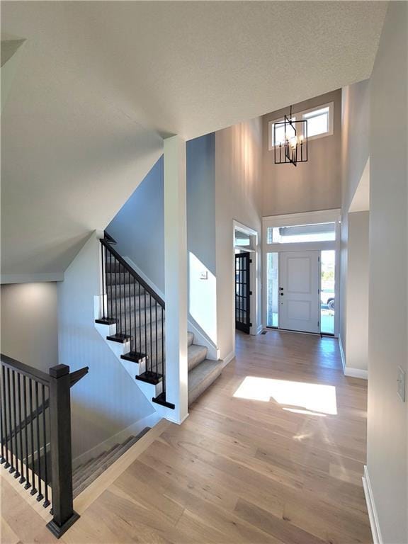 entrance foyer with baseboards, a towering ceiling, wood finished floors, and a notable chandelier
