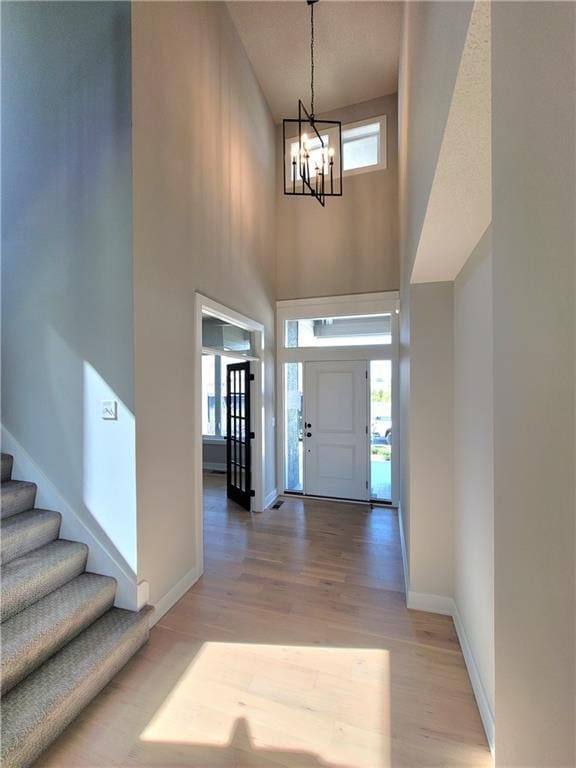 foyer entrance featuring a towering ceiling, light wood-type flooring, stairway, baseboards, and a chandelier