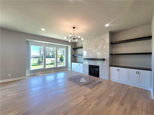 unfurnished living room with light wood-type flooring, recessed lighting, baseboards, and a notable chandelier