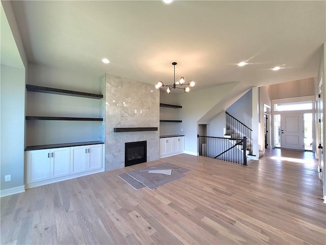 unfurnished living room with built in shelves, wood finished floors, baseboards, a chandelier, and stairs