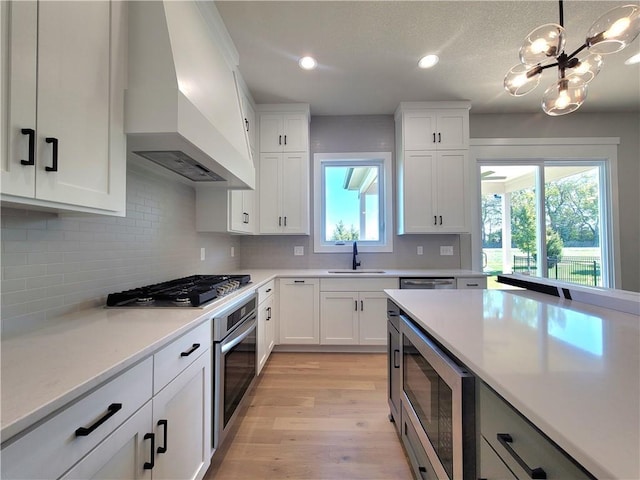 kitchen with appliances with stainless steel finishes, a sink, light countertops, light wood-style floors, and custom range hood