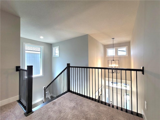 hall with carpet floors, a textured ceiling, a chandelier, baseboards, and an upstairs landing