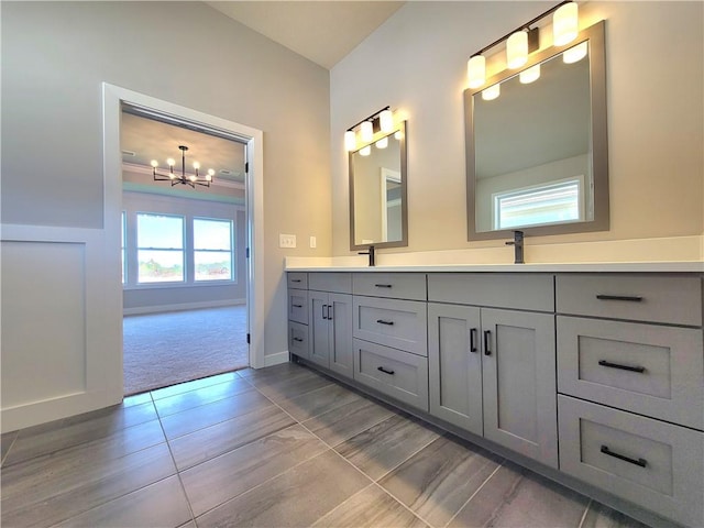full bathroom featuring an inviting chandelier, double vanity, a sink, and baseboards