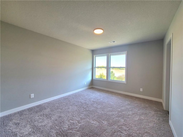 carpeted spare room featuring a textured ceiling, visible vents, and baseboards