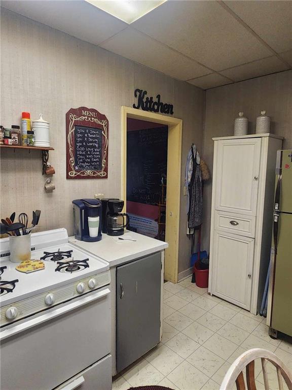 kitchen with white range with gas stovetop, light countertops, a drop ceiling, and freestanding refrigerator