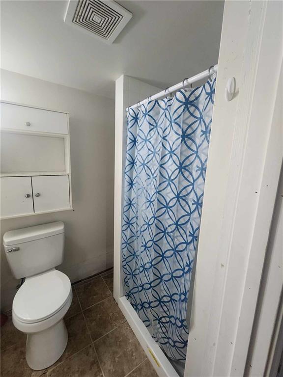 bathroom with tile patterned floors, toilet, visible vents, and a shower stall