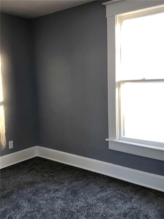 spare room featuring dark colored carpet, plenty of natural light, and baseboards