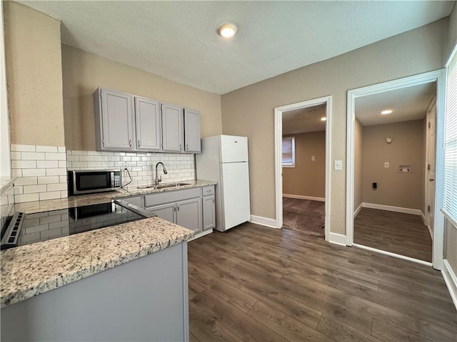 kitchen with white fridge, sink, backsplash, dark hardwood / wood-style floors, and light stone counters