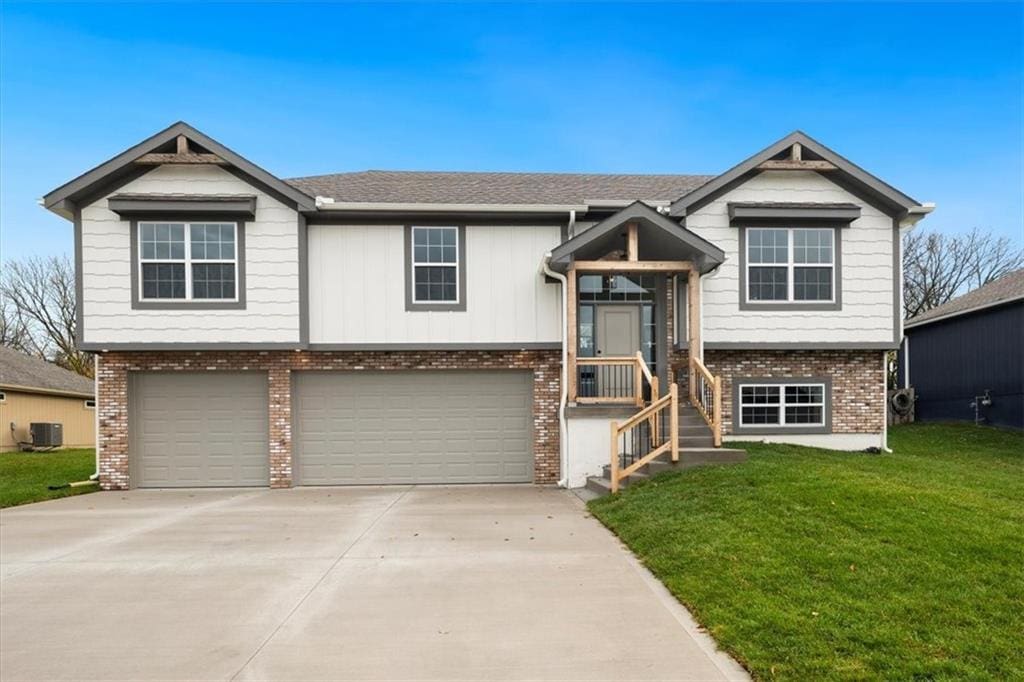 raised ranch featuring a garage, cooling unit, and a front yard