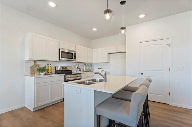 kitchen featuring sink, hanging light fixtures, stainless steel appliances, an island with sink, and white cabinets