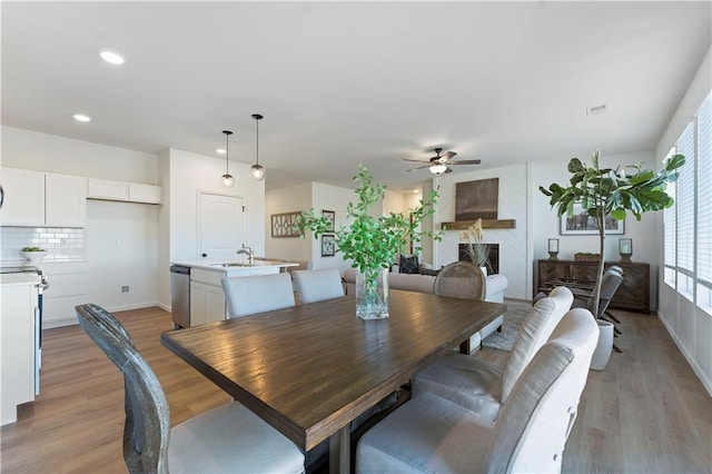 dining space featuring ceiling fan, a large fireplace, sink, and light hardwood / wood-style flooring