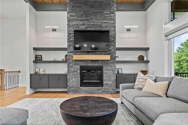 living room with light hardwood / wood-style floors, a stone fireplace, and wooden ceiling