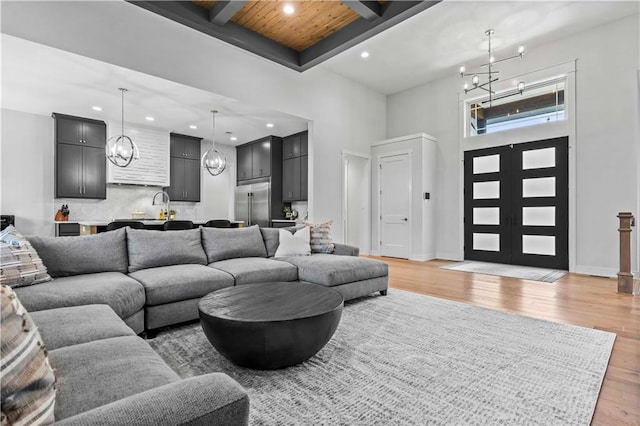 living room featuring beamed ceiling, french doors, light wood-type flooring, a high ceiling, and wood ceiling