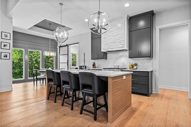 kitchen with a kitchen breakfast bar, light hardwood / wood-style flooring, decorative backsplash, hanging light fixtures, and a kitchen island with sink