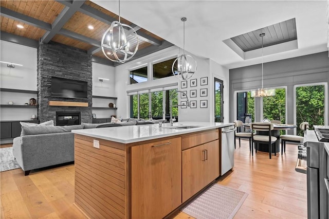 kitchen with a fireplace, light wood-type flooring, an island with sink, hanging light fixtures, and coffered ceiling