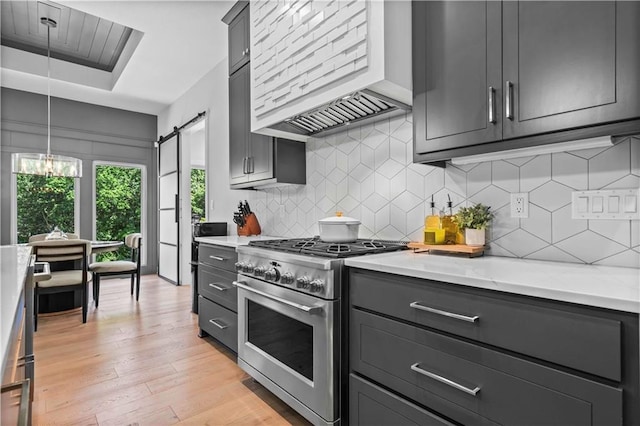 kitchen featuring premium range hood, stainless steel stove, light hardwood / wood-style flooring, pendant lighting, and a barn door